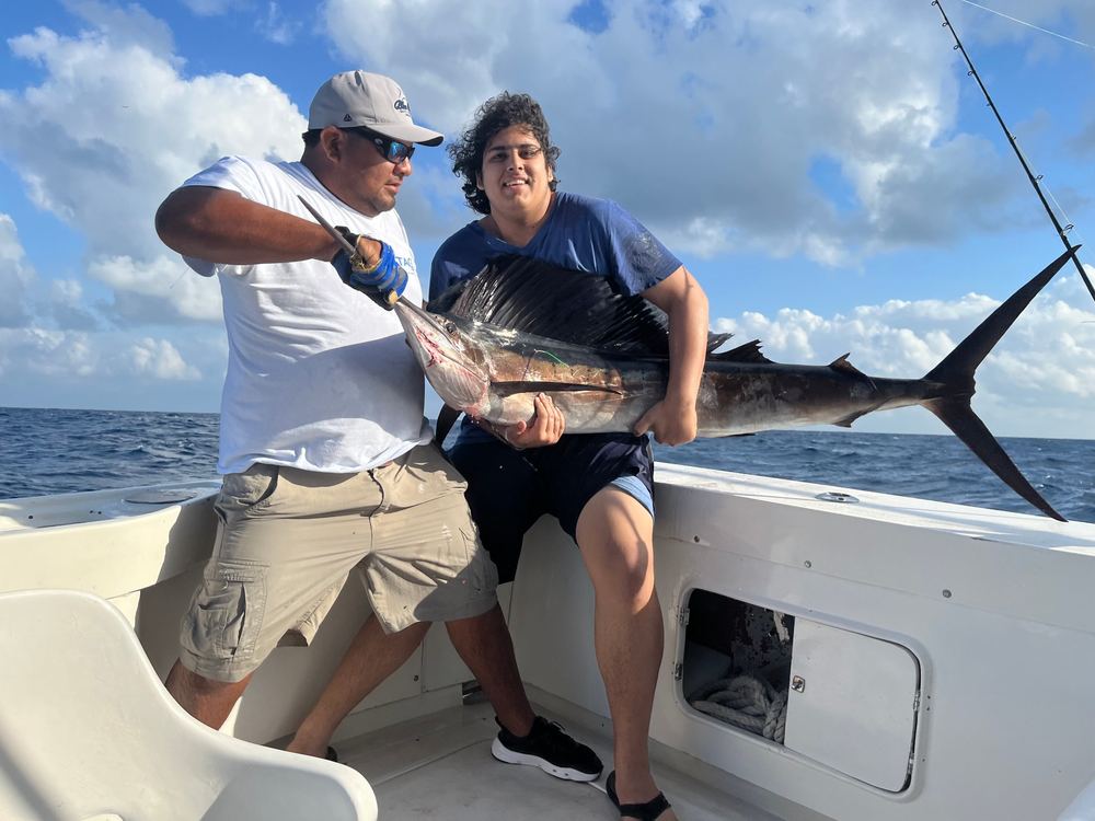 Gabriel and the boat's mate holding a sailfish on deck, open ocean behind