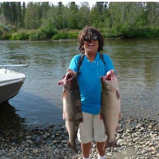 A young Gabriel on a gravel riverbank holding two salmon