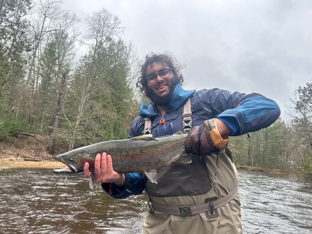 Gabriel in waders holding a steelhead in a river under grey skies