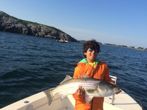 A young Gabriel on a boat holding a striped bass, a rocky island behind